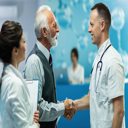 Happy mature businessman shaking hands with doctor in the hospital. male-doctor-handshaking-while-greeting-hallway-clinic